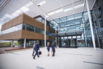 Forretningsfolk går ind i en moderne kontorbygning med glasfacade og overdækket indgang.