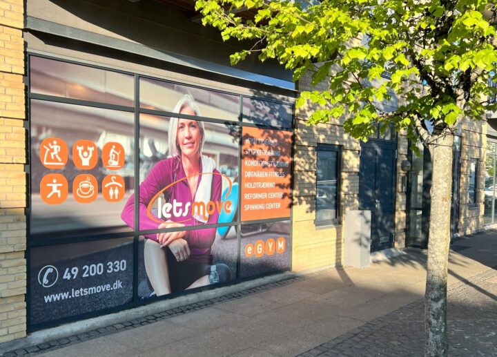 Facade af Letsmove fitnesscenter med reklamevinduer, træer i forgrunden og tydelig branding.